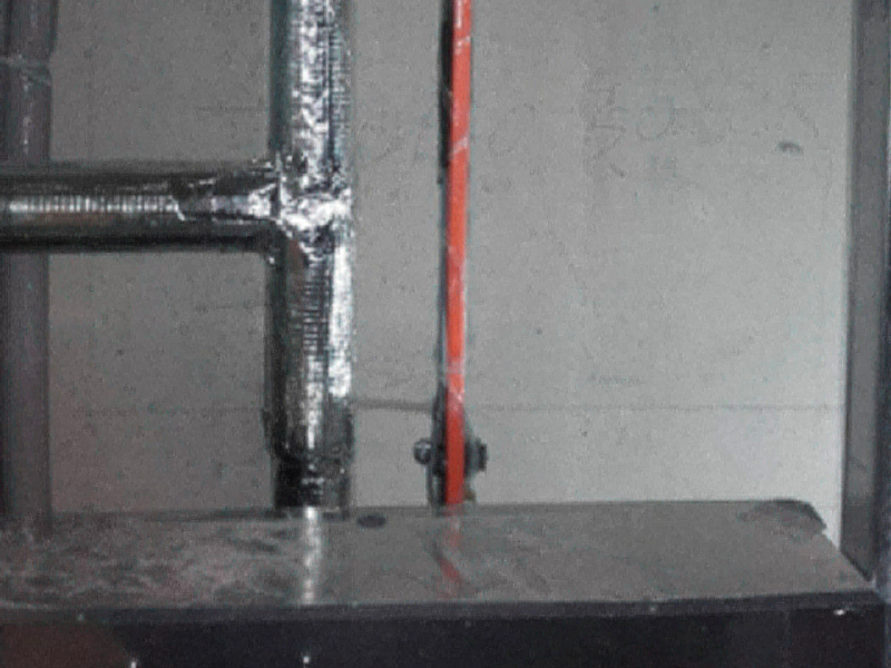 Gedämmte Rohrleitung neben einer roten Leitung an einer Betonwand